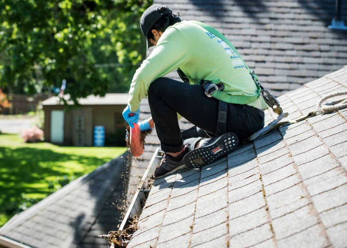 Worker wearing a green long sleeved shirt cleaning the gutter