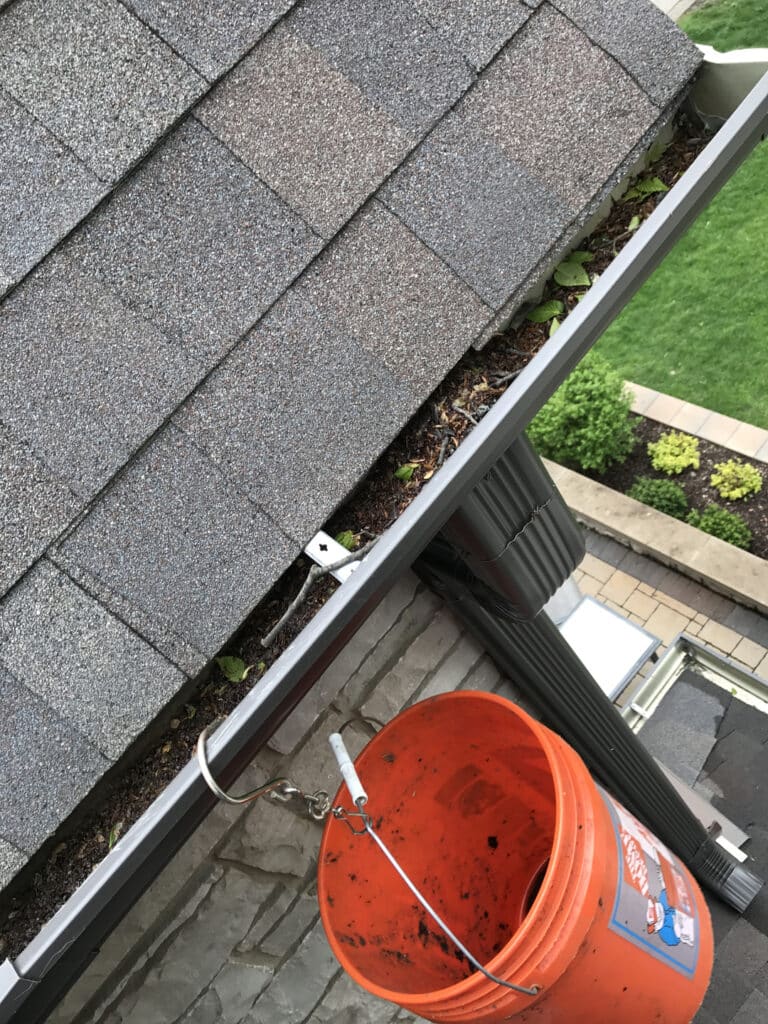 Orange bucket is hooked on roof's gutter. Residential gutter clear