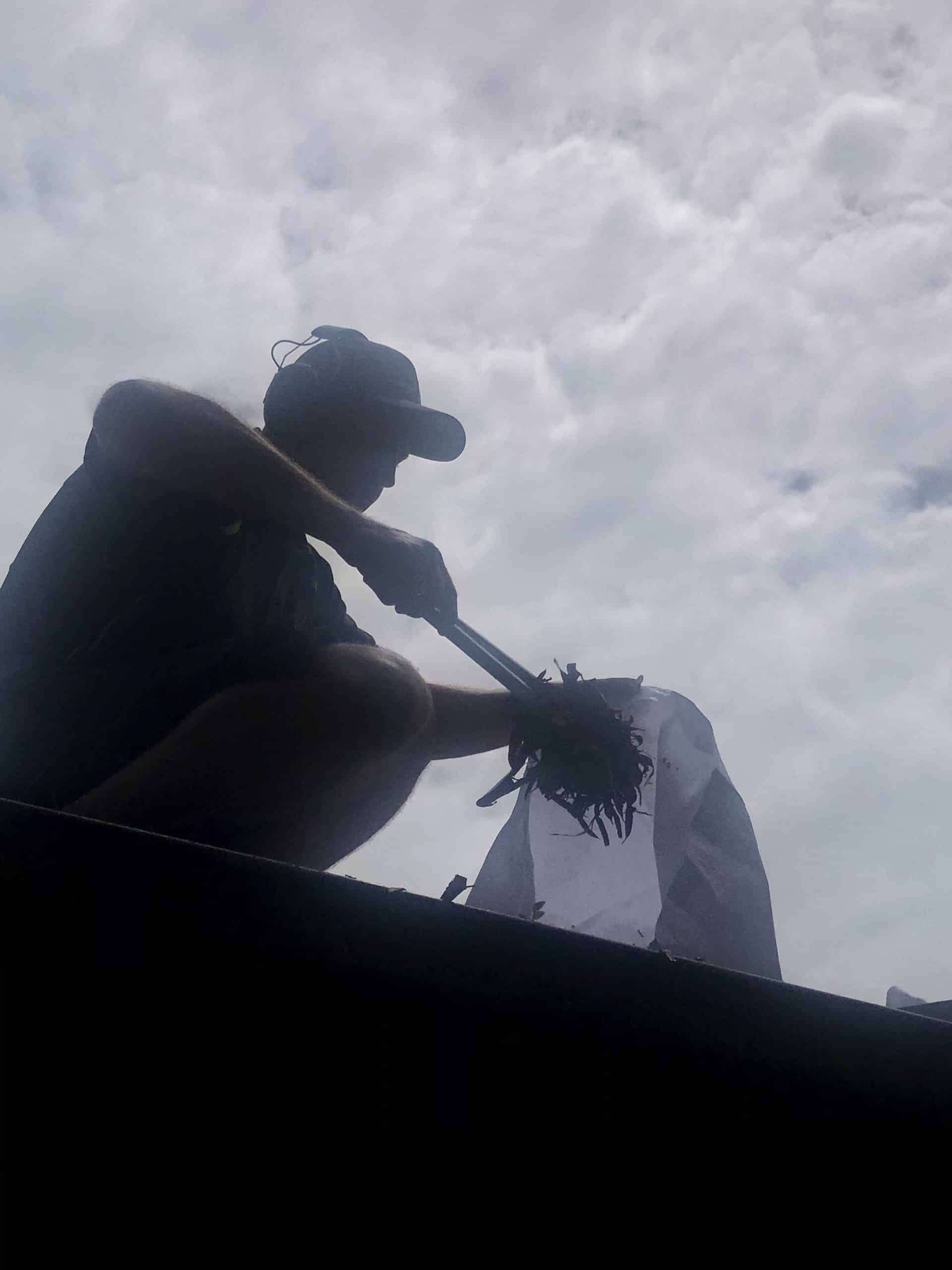 Worker scraping the leaves in a gutter using a tong